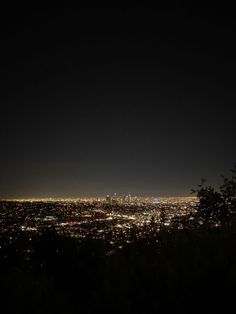 the city lights are lit up in the dark night sky from atop a hill at twilight