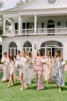 a group of women walking across a lush green field in front of a white building