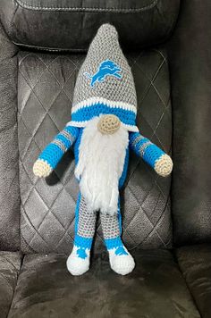 a crocheted blue and white gnome sitting in a gray chair with the detroit lions on it's back