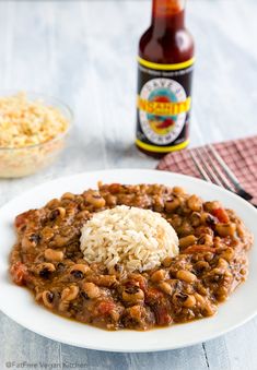 a white plate topped with beans and rice next to a bottle of hot dog sauce