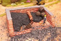 a toy man is standing in front of a brick wall with bricks and gravel surrounding it