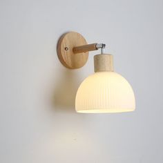 a white wall light with a wooden arm on a gray wall next to a lamp shade