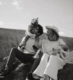 a man and woman sitting on top of a rock with a baby in their arms