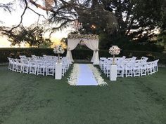 an outdoor ceremony setup with white chairs and flowers on the aisle, decorated with candles