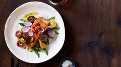 a white plate topped with fish and veggies on top of a wooden table