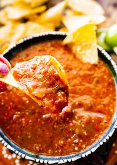 a hand holding a tortilla chip over a bowl of salsa