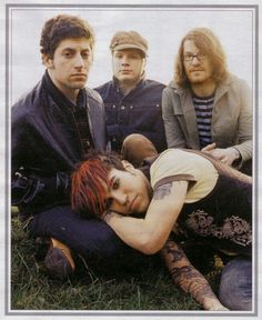 four people sitting in the grass with one woman laying on her chest and two men standing behind them