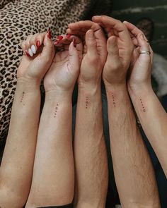 four people with matching tattoos on their arms holding each other's hands in the air