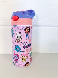 a pink and blue cup with cartoon characters on it sitting next to a white wall