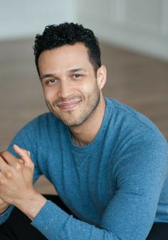 a man sitting on the floor with his hands folded in front of him smiling at the camera