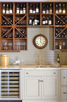 a wine cellar with lots of bottles and glasses on the shelves, along with a clock mounted to the wall