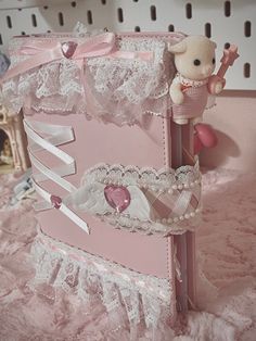 a teddy bear is sitting on top of a pink box with white lace and bows