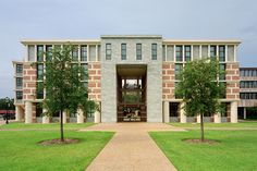 a large building with trees in front of it on a grassy field next to a sidewalk