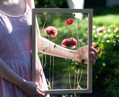 a woman holding up a piece of art with red flowers on it and grass in the background