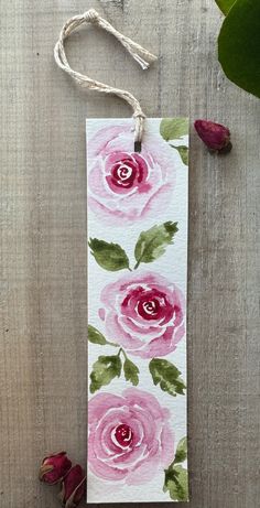 a tag with watercolor roses painted on it next to some dried flowers and twine