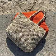 an orange purse sitting on top of a cement floor next to the ocean and sand