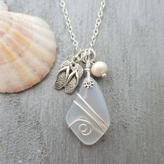 a sea glass necklace with charms on it next to a seashell and pearl bead