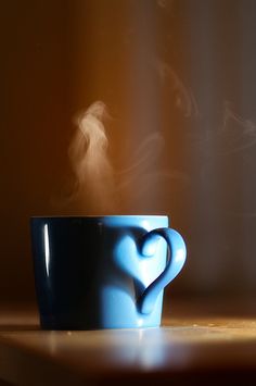 a blue coffee cup sitting on top of a wooden table with steam coming out of it