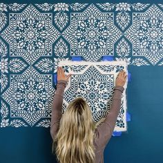 a woman is painting a wall with blue and white stencils on the walls