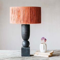 a table lamp sitting on top of a wooden table next to a vase with flowers in it