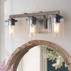 a bathroom vanity with three lights and a mirror on the wall next to vases