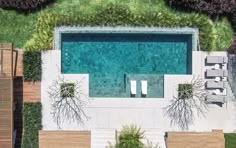 an aerial view of a swimming pool surrounded by greenery and wooden benches with chairs around it