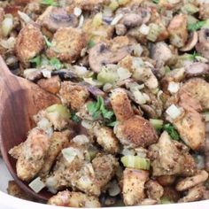 a wooden spoon is in a dish full of stuffing and vegetables with meat on top