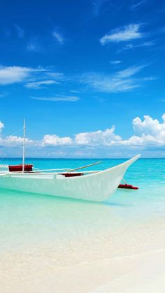 a white boat sitting on top of a sandy beach next to the ocean under a blue sky