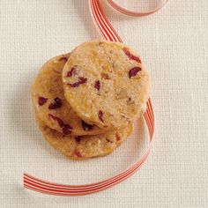 three cookies with cranberries are on a white tablecloth next to a red and white striped ribbon