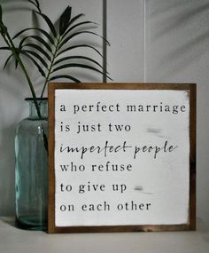 a wooden sign sitting on top of a table next to a vase filled with plants