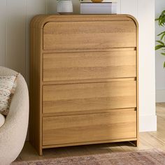 a wooden chest of drawers next to a chair and potted plant on top of it