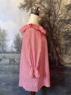 This charming Red Gingham Tunic Dress is perfect for cozy cottage mornings with it's historically-inspired features, such as a playful scalloped ruffle collar, scalloped ruffle bishop sleeves, an A-line silhouette, and wide hem. Wear it alone, or as a chemise for a full victorian-inspired outfit! This piece is a product sample that we did not order more of, and thus stock is limited to one! Sizing: Fits like an L-XLBust - up to 48 Inches / 125 CentimetersWaist - up to 48 Inches / 125 CentimetersLength - 31 Inches / 78 CentimetersSleeve Length - 21.5 Inches / 54 CentimetersSleeve Width - 19 Inches / 48 Centimeters Condition:A+ | New without tags. Product sample. Materials:100% Cotton Gingham Plaid Cotton Dress With Ruffles, Gingham Cotton Dress With Ruffle Hem, Gingham Tiered Ruffle Dress, Red Dress With Ruffles And Peter Pan Collar, Cottagecore Gingham Dress With Ruffles, Fantasy Shop, Countryside Cottage, Ruffle Collar, Red Gingham