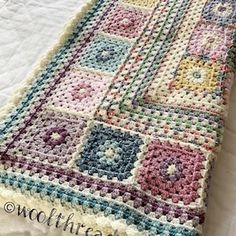 a crocheted blanket is laying on top of a white bed spread with colorful squares