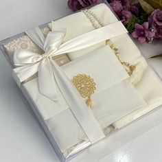 an open box with a necklace and bracelet in it next to purple flowers on a table