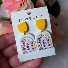 a pair of yellow and pink earrings on top of a white card with flowers in the background