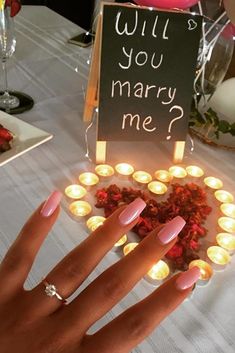 a woman's hand with pink nail polish holding up a sign that says will you marry me?