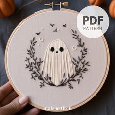 a hand embroidery pattern with a ghost in the middle and leaves around it, surrounded by pumpkins