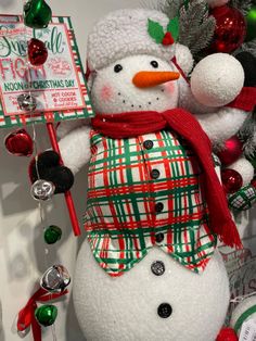 a snowman with a red hat and scarf next to a christmas tree filled with ornaments