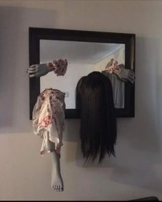 a creepy doll is standing in front of a mirror with her hair hanging from the wall