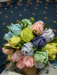 a bouquet of multicolored paper roses in a vase on a tablecloth covered table