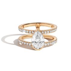 a gold ring with a pear shaped diamond on top and two rows of diamonds around the band