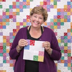 a woman holding up a piece of paper in front of a quilt