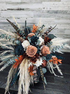 an arrangement of flowers and feathers on a wooden table with wood planks in the background