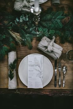 a place setting with silverware, napkins and pine cones on a wooden table