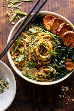 a bowl filled with noodles and vegetables next to chopsticks on a wooden table