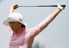 a woman in pink shirt and white hat holding up her golf club to hit the ball