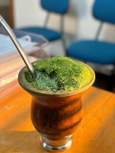 a cup filled with green liquid sitting on top of a wooden table next to a blue chair