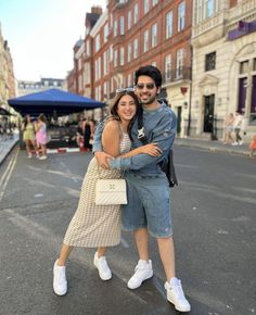 a man and woman standing in the middle of a street with buildings on both sides