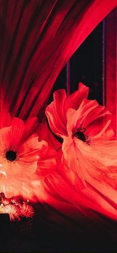 two red flowers sitting on top of a window sill next to a bed sheet