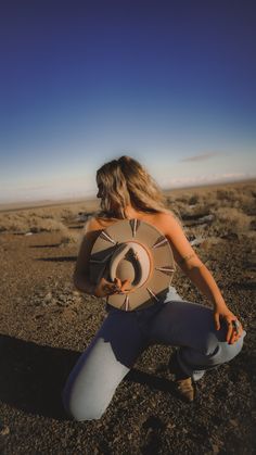 a woman kneeling down with a hat on her head in the middle of an open field